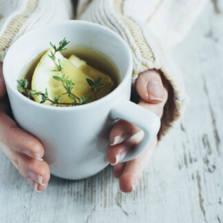 Human hands holding cup of tea with thyme herb and lemon slices on a wooden table,.